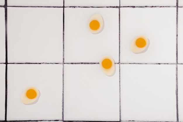 Concept de cuisine créative avec des bonbons gommeux jaunes en forme d'oeuf frit sur fond de comptoir de carreaux de cuisine blanc et noir Vue de dessus du petit déjeuner du matin Modèle sans couture style minimal Pose plate
