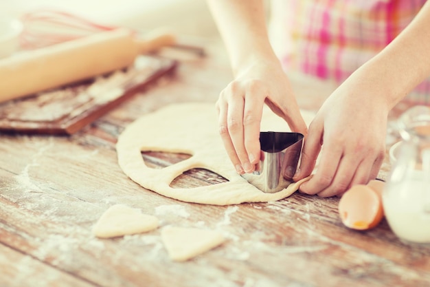Concept de cuisine et de la maison - gros plan des mains féminines faisant des biscuits à partir de pâte fraîche à la maison