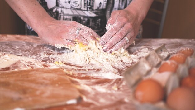 Concept de cuisine et de maison - gros plan sur des mains féminines pétrissant la pâte à la maison. Flou artistique