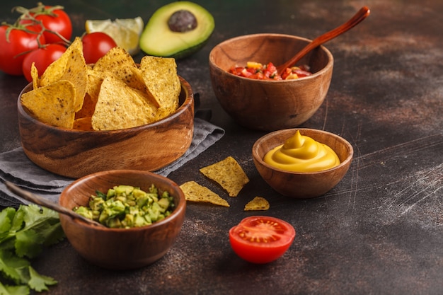 Concept de cuisine mexicaine Nachos - chips de totopos au maïs jaune avec diverses sauces dans des bols en bois: guacamole, sauce au fromage, pico del gallo, espace de copie