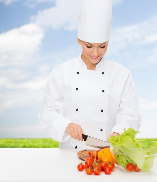 concept de cuisine et de nourriture - femme chef souriante, hacher des légumes