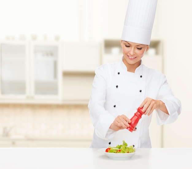 concept de cuisine et de nourriture - femme chef souriante préparant une salade avec un moulin à sel ou à poivre