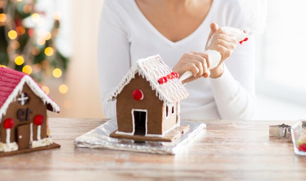 concept de cuisine, de personnes, de noël et de décoration - femme heureuse faisant des maisons en pain d'épice à la maison