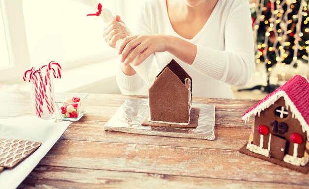 concept de cuisine, de personnes, de noël et de décoration - femme heureuse faisant des maisons en pain d'épice à la maison