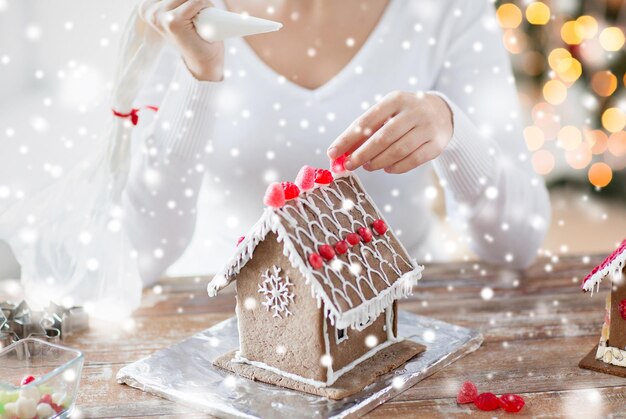 concept de cuisine, de personnes, de noël et de décoration - gros plan d'une femme heureuse faisant des maisons en pain d'épice à la maison