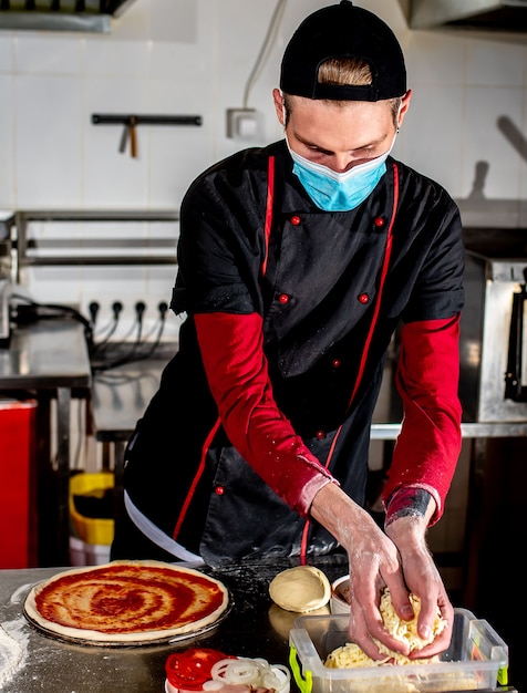 Concept de cuisine de pizza, chef en masque médical mettant la pâte de tamat sur la pizza