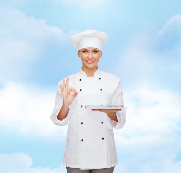 concept de cuisine, de technologie et de personnes - chef féminin souriant, cuisinier ou boulanger avec ordinateur tablette pc sur fond bleu ciel nuageux
