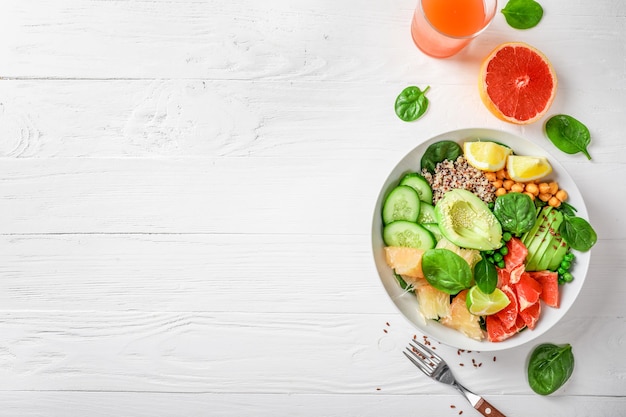 Concept de cuisine végétalienne : quinoa à l'avocat, concombres, pois verts, pois chiches, épinards et agrumes sur fond blanc. Vue de dessus.