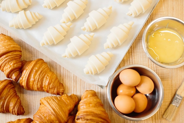 Concept de cuisson des croissants Des croissants crus enroulés et fraîchement cuits ainsi que des ingrédients se trouvent sur la table