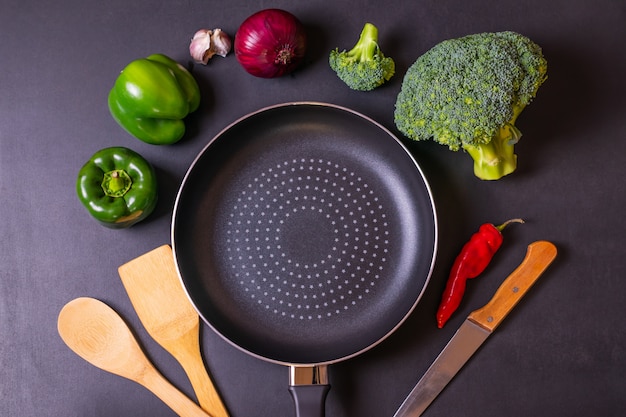 Concept de cuisson fond noir avec poêle, brocoli frais, poivrons, oignons rouges et ail.