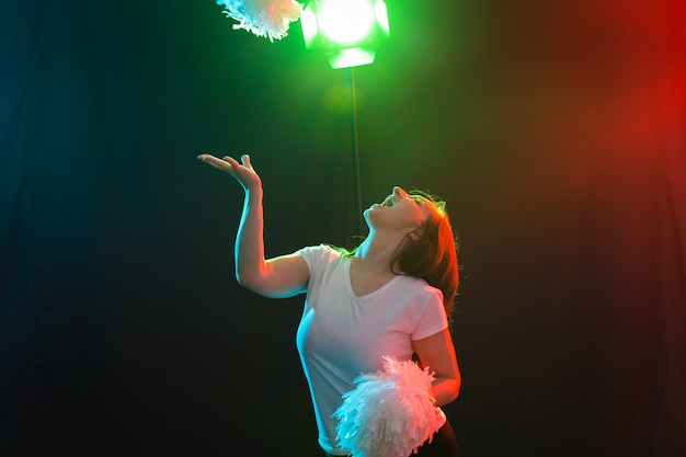 Concept de danse, de sport et de personnes - jolie jeune femme dansant dans l'obscurité avec des pompons et souriante.