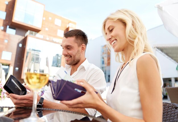 concept de date, de personnes, de paiement et de finances - couple heureux avec portefeuille et verres à vin payant la facture au restaurant