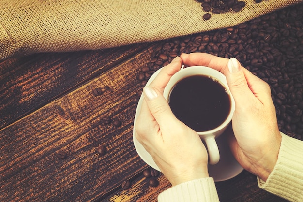 Concept de dégustation de café dans un style rustique la femme tient une tasse de café dans ses mains sur une table en bois avec des grains renversés d'un effet vintage de sac de toile de jute
