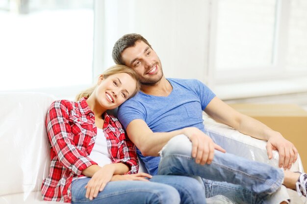 concept de déménagement, de maison et de couple - couple souriant se reposant sur un canapé dans une nouvelle maison