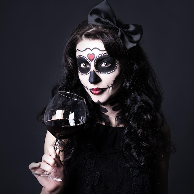 Concept de dépendance à l'alcool femme avec crâne d'Halloween maquillage tenant un verre de vin ou de sang sur fond noir