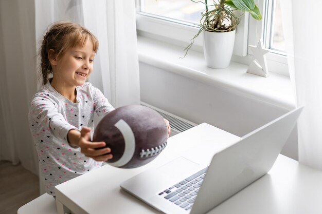 Concept de dépendance à Internet et d'ordinateurs avec enfant et ordinateur portable, petite fille avec ballon de rugby