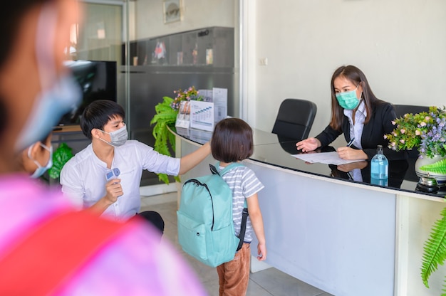 Concept de dépistage Covid-19 aux étudiants. L'enseignant a accueilli les élèves et dépisté l'infection à coronavirus, pris la température corporelle et pris la fièvre de l'élève le matin avant le cours.