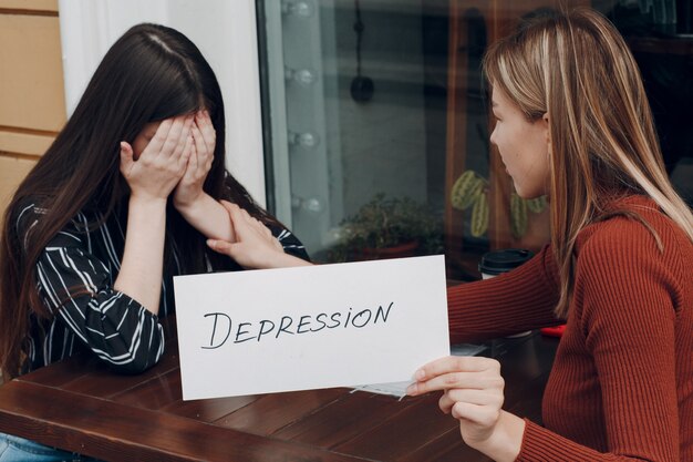 Concept de dépression cachée. Femme qui pleure. Deuxième femme tenant une feuille de papier blanc étiqueté le mot dépression à la main. Deux femmes parlant au café de la rue.