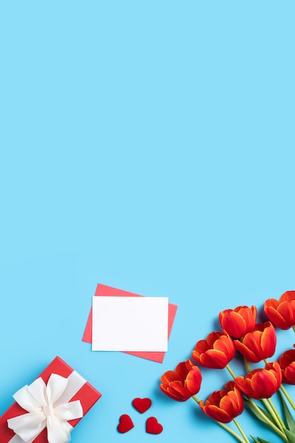 Concept de design de cadeau de voeux de vacances de fête des mères avec bouquet de tulipes rouges et carte sur fond de table bleu clair