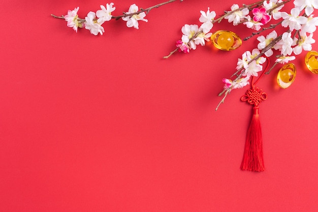 Concept de design du nouvel an lunaire chinois - beau noeud chinois avec fleur de prunier isolé sur fond rouge, mise à plat, vue de dessus, mise en page.