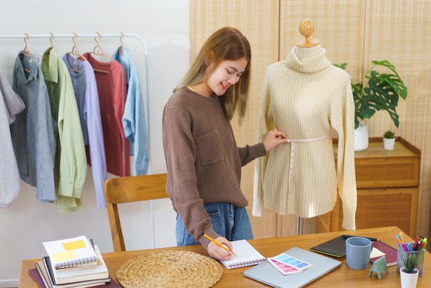 Concept de design de mode Créateur de mode mesurant le chandail dans le mannequin et prenant des notes pour le contrôle