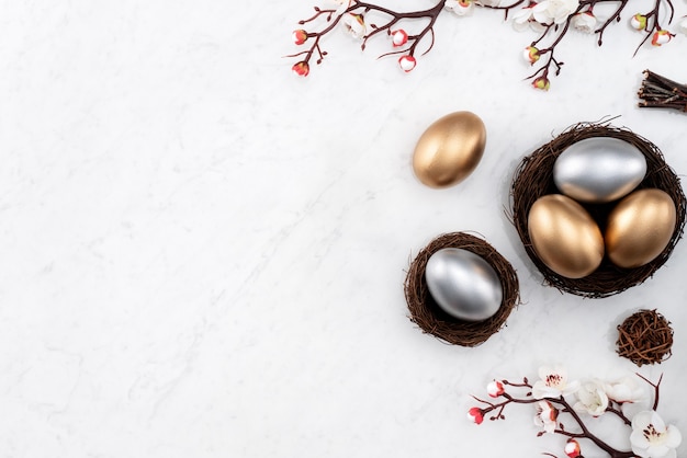 Concept de design d'oeufs de Pâques d'or et d'argent dans le nid avec fleur de prunier blanc sur fond de table en marbre blanc brillant.