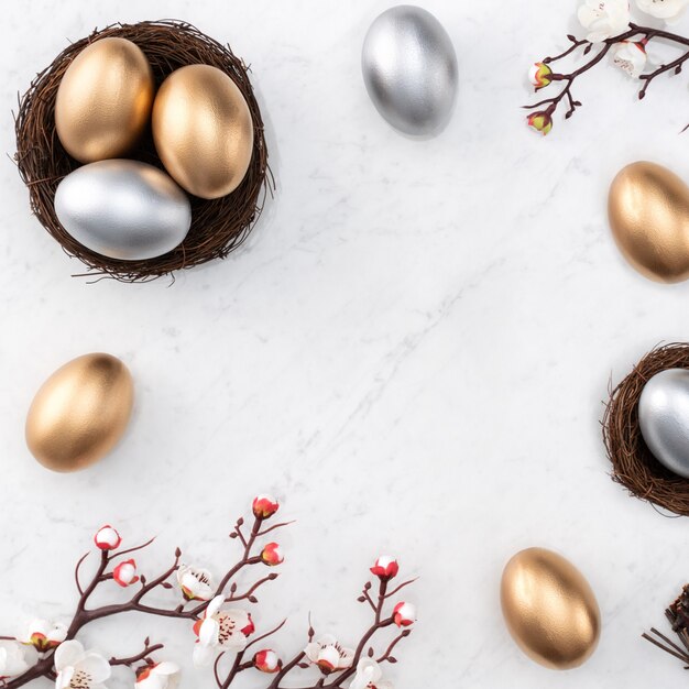 Concept de design d'oeufs de Pâques d'or et d'argent dans le nid avec fleur de prunier blanc sur fond de table en marbre blanc brillant.