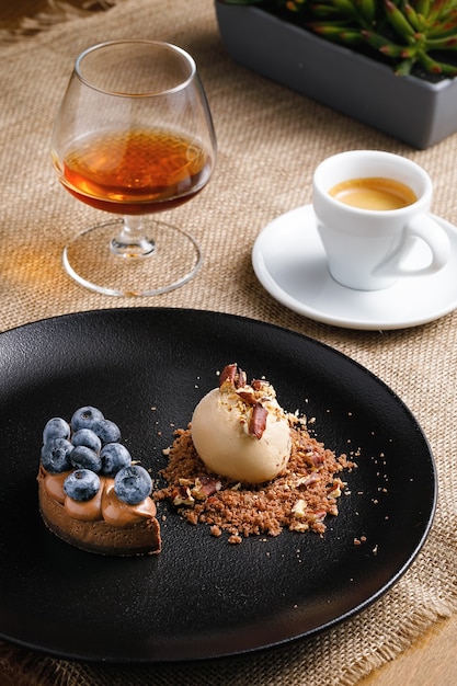 Concept de dessert, crème glacée et petit gâteau aux fruits rouges sur une plaque noire, café au brandy sur la table.