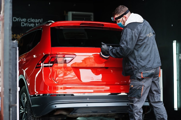 Concept de détail de voiture. Homme au masque facial avec polisseur orbital en atelier de réparation polissage voiture suv orange.