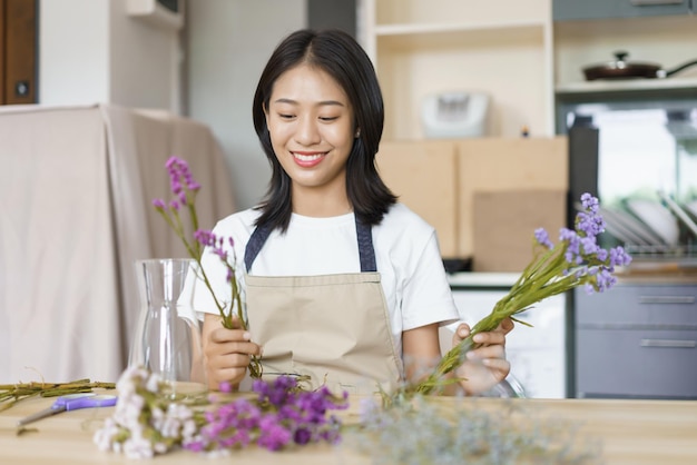 Concept de détente à domicile Jeune femme assise dans la salle de cuisine et arranger des fleurs dans un vase sur la table