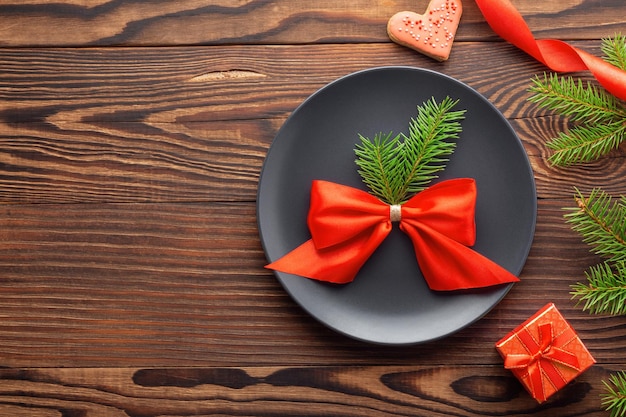 Photo concept de dîner de noël avec arc rouge sur plaque noire et brindilles d'épinette sur fond de bois rural, vue de dessus, espace vide