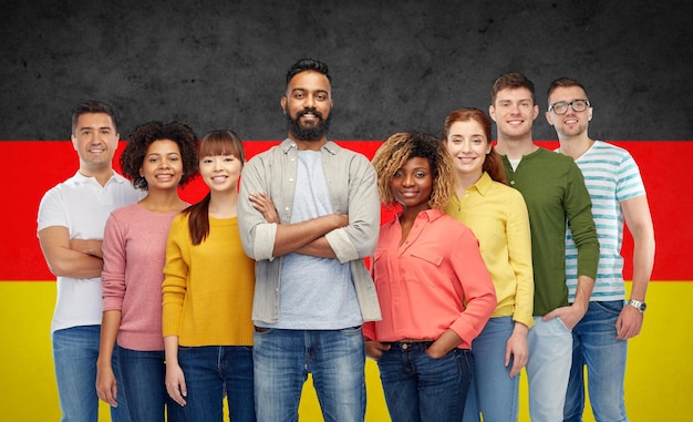 concept de diversité, d'immigration, d'ethnicité et de personnes - groupe international d'hommes et de femmes souriants heureux sur fond de drapeau allemand