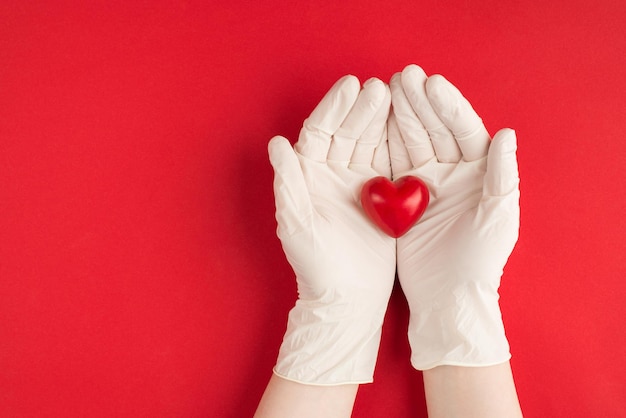 Concept de dons médicaux. Haut au-dessus de la vue aérienne photo de mains féminines dans des gants blancs tenant un coeur rouge isolé sur fond rouge avec fond