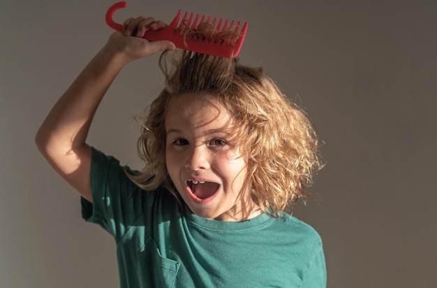 Photo le concept du peigne et de la brosse à cheveux, le garçon fait des expressions faciales en peignant les cheveux, l'enfant avec la blonde enchevêtrée.