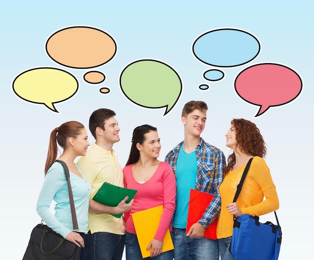 Photo concept d'école, d'éducation, de communication et de personnes - groupe d'étudiants souriants avec des dossiers et des sacs d'école sur fond bleu avec des bulles de texte