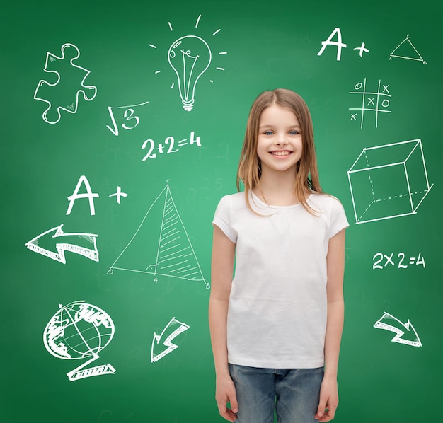 concept d'école, d'enfance et d'éducation - petite fille souriante en t-shirt blanc vierge sur fond de tableau vert