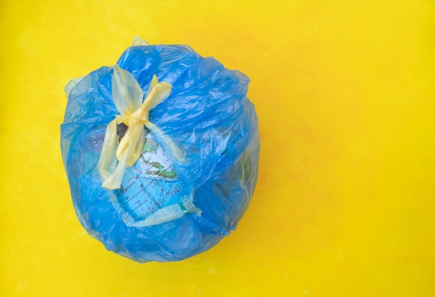 Photo le concept d'écologie et de protection de la nature un globe dans un sac poubelle sur fond jaune avec une place pour le texte poster