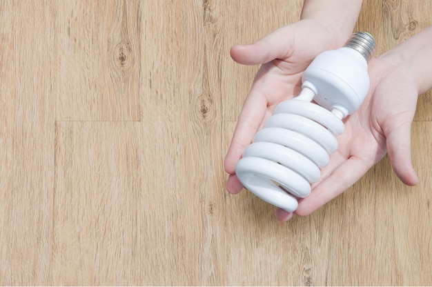 Concept d'économie d'énergie Main de femme tenant une ampoule sur fond de boisIdées ampoule dans la main