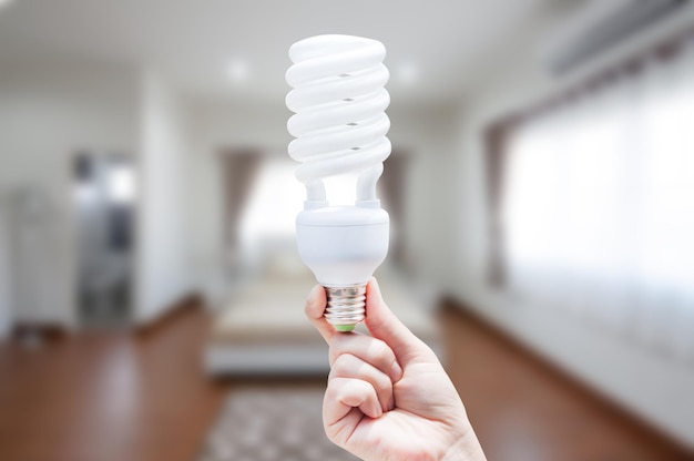 Concept d'économie d'énergie, main de femme tenant une ampoule sur fond de chambre, ampoule d'idées dans la main