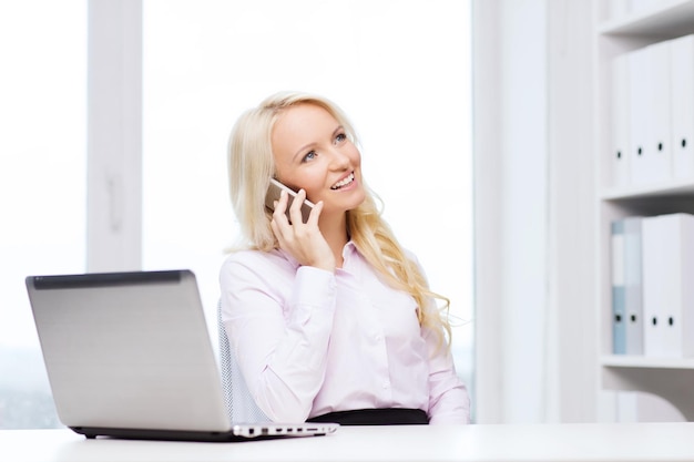 concept d'éducation, d'affaires, de communication et de technologie - femme d'affaires souriante ou étudiante avec ordinateur portable appelant sur smartphone au bureau