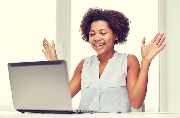 Photo concept d'éducation, d'affaires, de succès et de technologie - femme d'affaires ou étudiante afro-américaine heureuse avec ordinateur portable et papiers au bureau