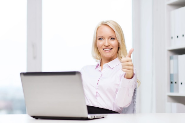 concept d'éducation, d'affaires et de technologie - femme d'affaires souriante ou étudiante montrant les pouces vers le haut avec un ordinateur portable au bureau