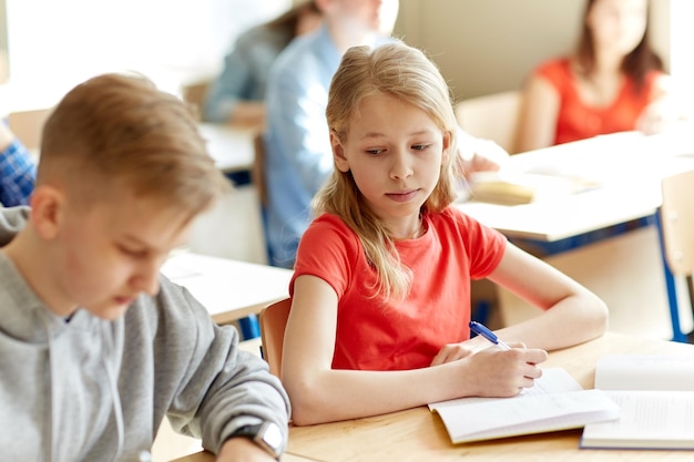 concept d'éducation, d'apprentissage et de personnes - groupe d'étudiants avec des livres écrivant un test scolaire et une fille qui triche