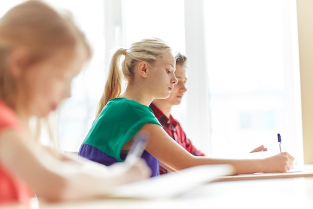 concept d'éducation, d'apprentissage et de personnes - groupe d'étudiants avec des livres écrivant un test scolaire