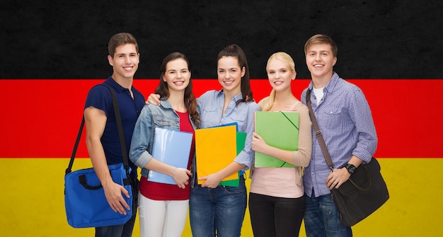 concept d'éducation, d'apprentissage et de personnes - groupe d'étudiants souriants avec des dossiers et des sacs d'école sur fond de drapeau allemand