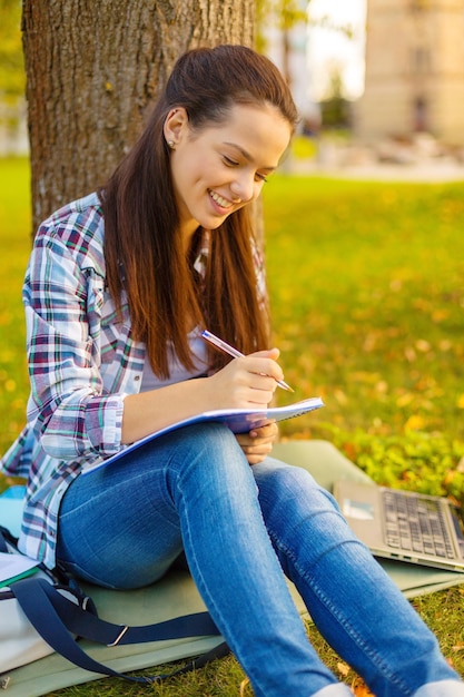 concept d'éducation, de campus et de personnes - adolescent souriant écrivant dans un cahier