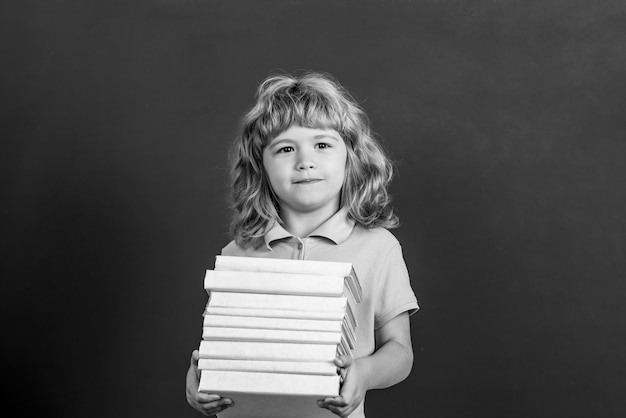 Concept d'éducation et de créativité Enfant tenant une pile de livres avec planche de mortier sur tableau noir Retour à l'école Écolier en classe Noir et blanc