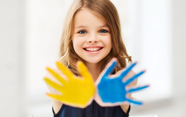 concept d'éducation, d'école, d'art et de bonheur - petite étudiante montrant les mains en jaune et bleu à l'école