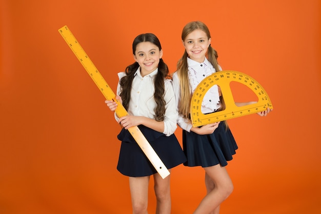 Concept d'éducation et d'école. Des écoliers apprennent la géométrie. Uniforme scolaire pour enfants sur fond orange. Disciplines scolaires STEM. Élève de jolies filles avec de grandes règles. Sujet de prédilection pour la géométrie.