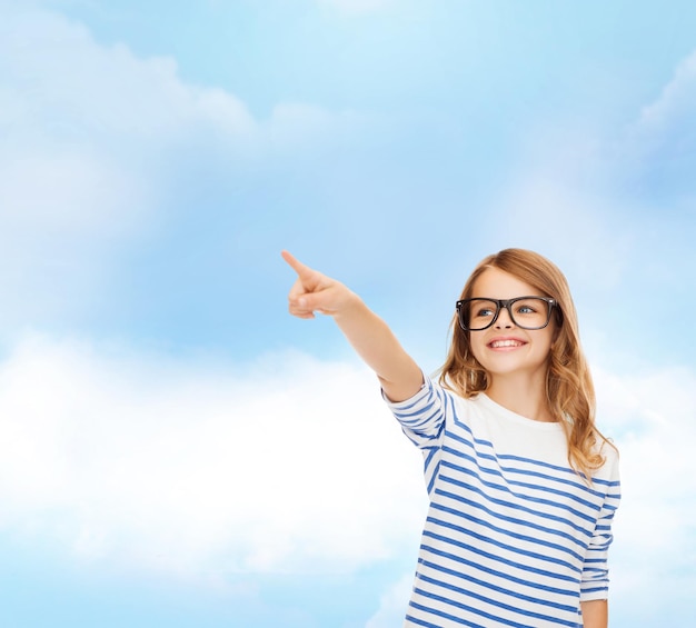 concept d'éducation, d'école et d'écran imaginaire - jolie petite fille à lunettes pointant dans l'air ou un écran imaginaire